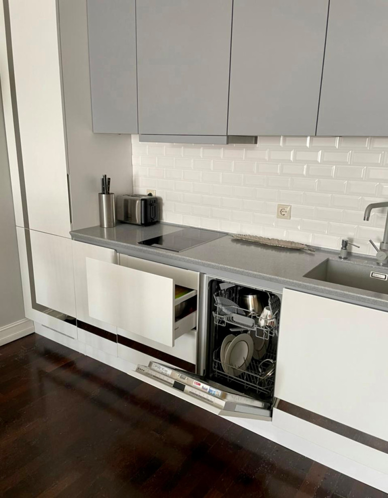 Photo of a mid-sized contemporary single-wall eat-in kitchen in Moscow with an undermount sink, beaded inset cabinets, white cabinets, solid surface benchtops, white splashback, ceramic splashback, stainless steel appliances, dark hardwood floors, with island, brown floor and grey benchtop.