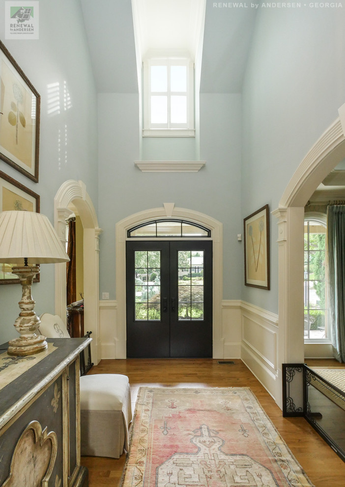 Großes Foyer mit blauer Wandfarbe, braunem Holzboden, Doppeltür, schwarzer Haustür, gewölbter Decke und vertäfelten Wänden in Atlanta