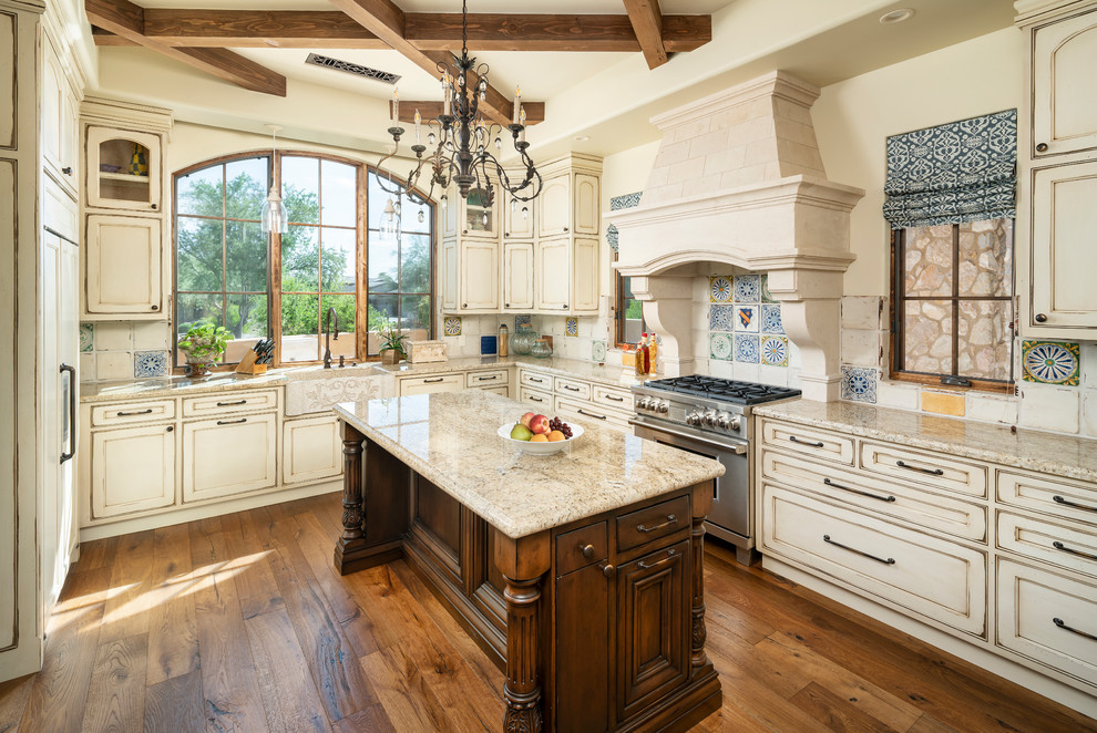Design ideas for a traditional u-shaped kitchen in Phoenix with a farmhouse sink, recessed-panel cabinets, distressed cabinets, beige splashback, stainless steel appliances, medium hardwood floors, brown floor and beige benchtop.