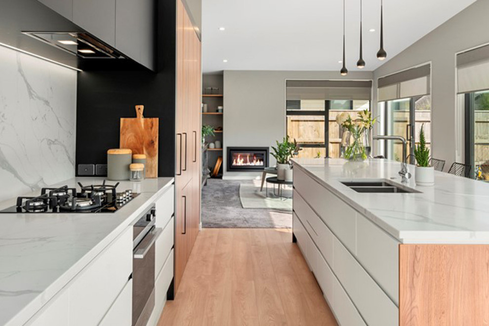Inspiration for a large galley open plan kitchen in Wellington with a double-bowl sink, flat-panel cabinets, medium wood cabinets, marble benchtops, white splashback, marble splashback, white appliances, light hardwood floors, with island, brown floor and blue benchtop.