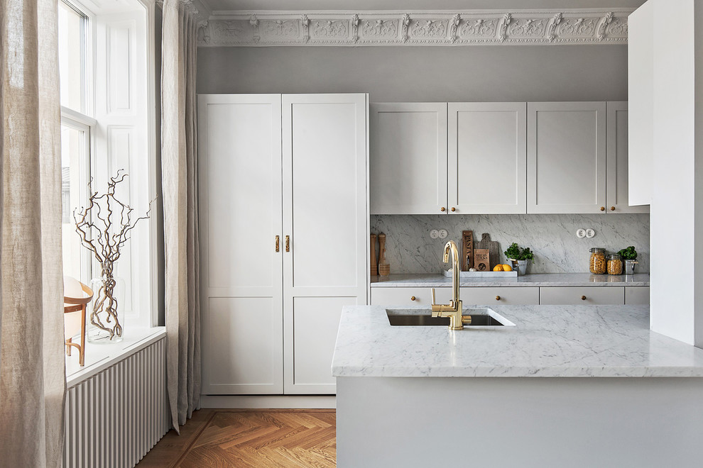 This is an example of a mid-sized scandinavian galley kitchen in Stockholm with an undermount sink, shaker cabinets, white cabinets, white splashback, medium hardwood floors, marble benchtops and no island.