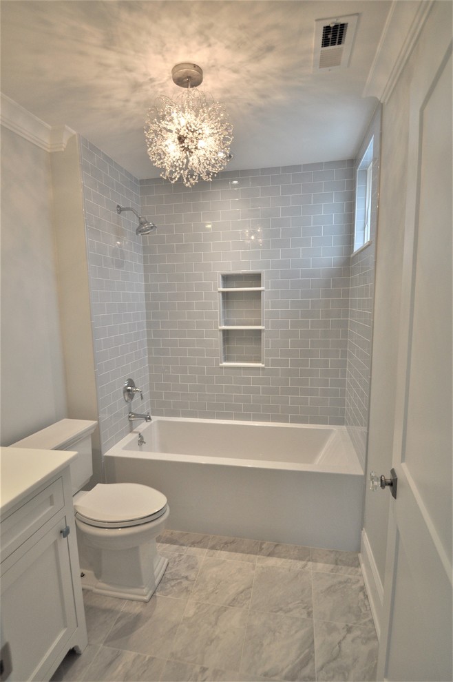 This is an example of a small transitional 3/4 bathroom in New York with shaker cabinets, white cabinets, an alcove tub, a shower/bathtub combo, a two-piece toilet, gray tile, subway tile, grey walls, marble floors, marble benchtops, grey floor and white benchtops.