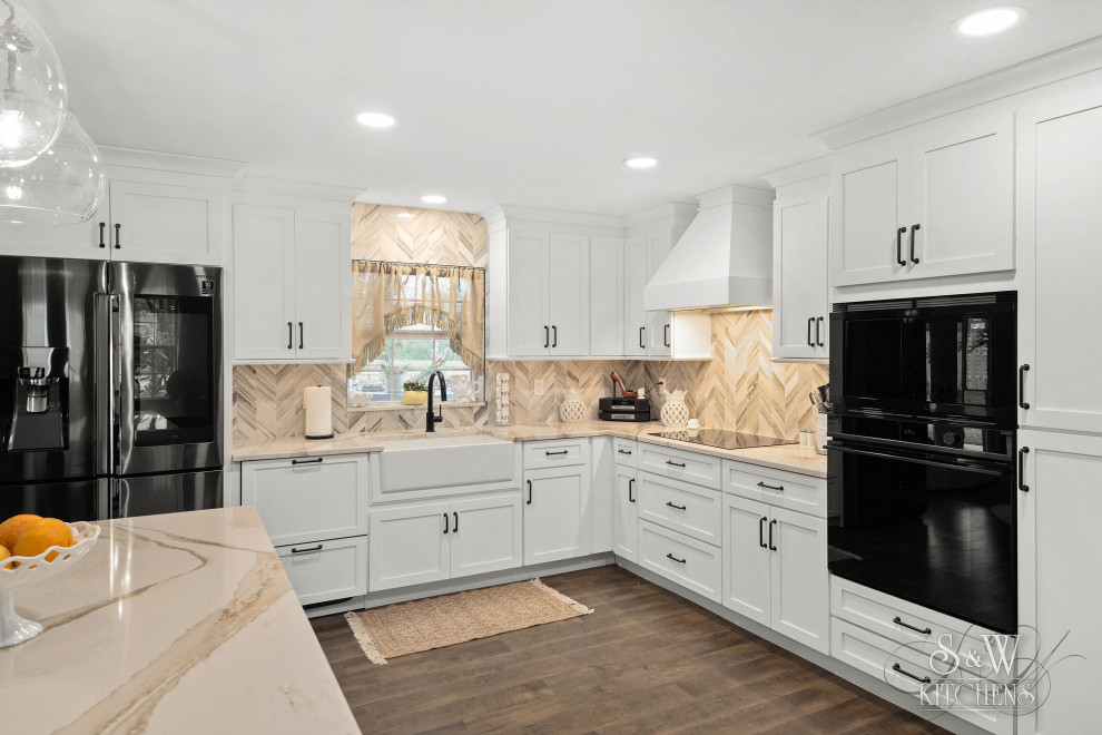 Inspiration for a mid-sized country l-shaped eat-in kitchen in Tampa with a farmhouse sink, shaker cabinets, white cabinets, quartz benchtops, beige splashback, marble splashback, black appliances, vinyl floors, with island, brown floor and beige benchtop.