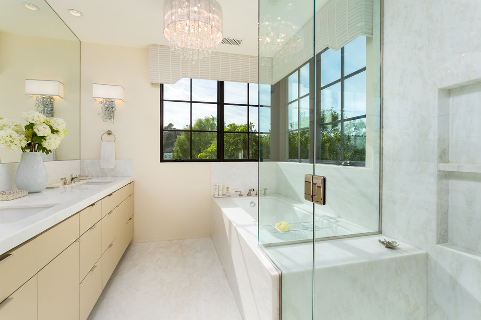 This is an example of a mid-sized mediterranean master bathroom in Los Angeles with flat-panel cabinets, yellow cabinets, an undermount tub, a corner shower, a one-piece toilet, white tile, marble, beige walls, marble floors, an undermount sink, marble benchtops, white floor and a hinged shower door.