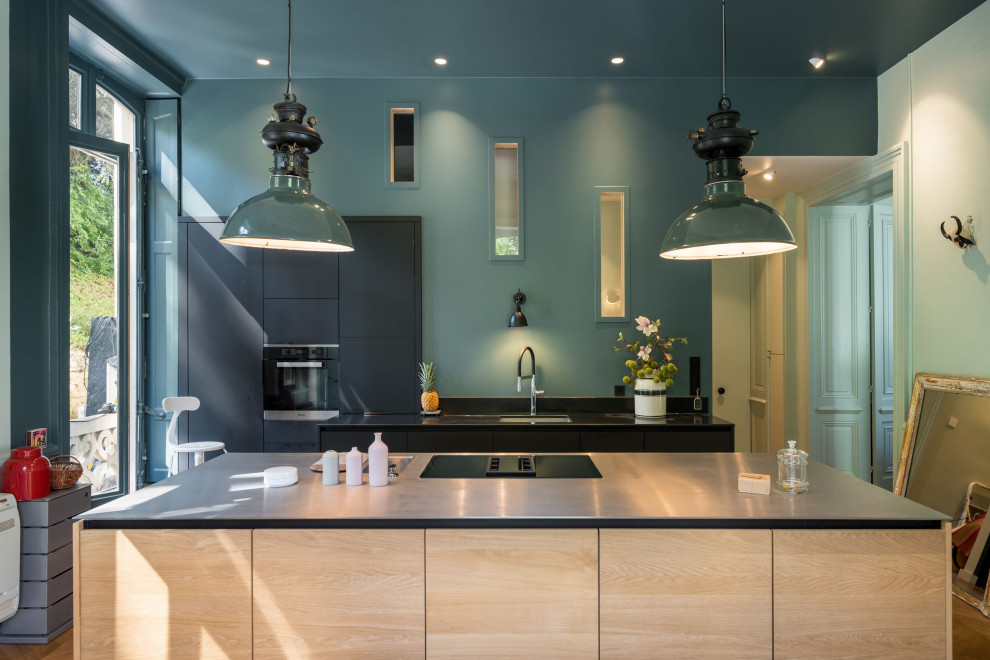 Large contemporary galley kitchen/diner in Lyon with a submerged sink, flat-panel cabinets, black cabinets, stainless steel appliances, medium hardwood flooring, an island, brown floors and black worktops.