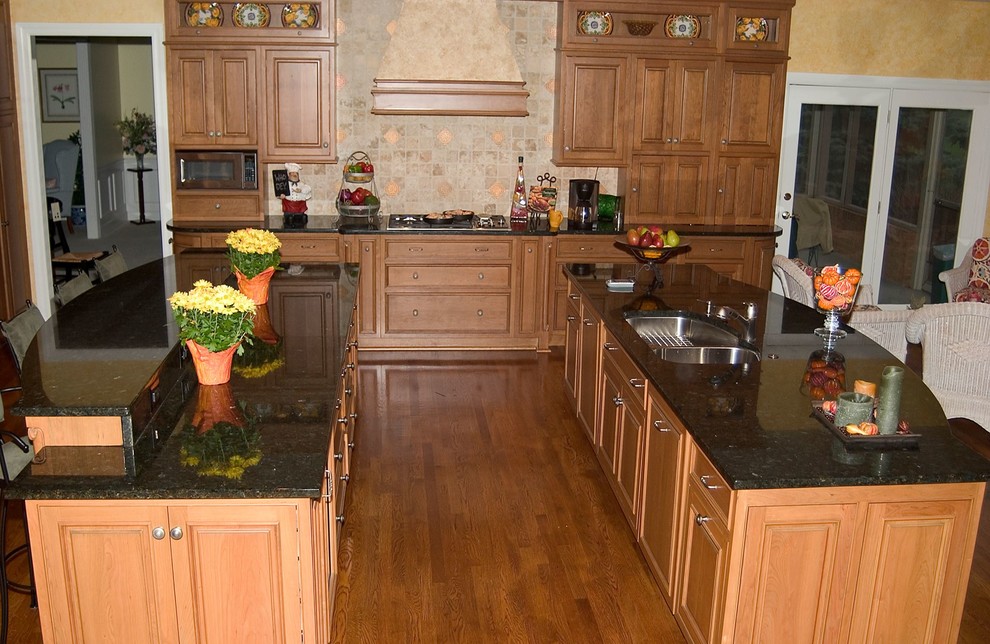 Inspiration for a large transitional u-shaped medium tone wood floor open concept kitchen remodel in Cincinnati with an undermount sink, raised-panel cabinets, light wood cabinets, granite countertops, beige backsplash, ceramic backsplash, paneled appliances and two islands