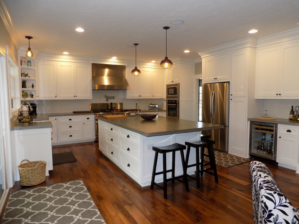 Large contemporary u-shaped eat-in kitchen in Columbus with a farmhouse sink, recessed-panel cabinets, white cabinets, concrete benchtops, white splashback, ceramic splashback, stainless steel appliances, medium hardwood floors and with island.