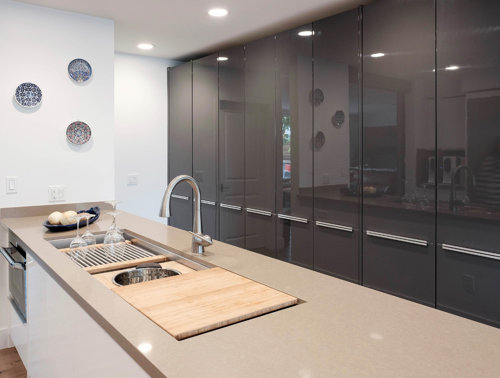 Photo of a large contemporary galley eat-in kitchen in Los Angeles with a drop-in sink, flat-panel cabinets, white cabinets, quartz benchtops, stainless steel appliances, light hardwood floors, a peninsula and brown floor.