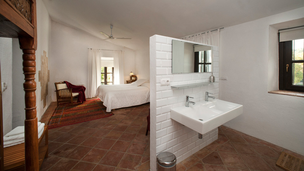 This is an example of a large country master bedroom in Seville with white walls and terra-cotta floors.