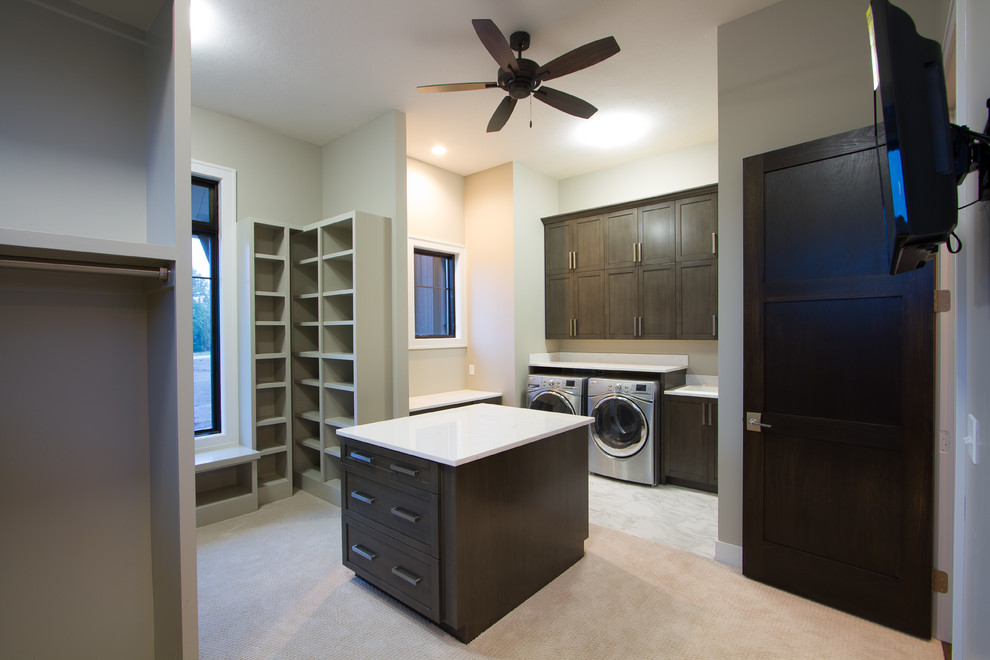 Photo of a large transitional u-shaped utility room in Omaha with shaker cabinets, dark wood cabinets, solid surface benchtops, beige walls, carpet and a side-by-side washer and dryer.