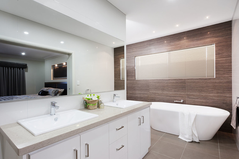 This is an example of a traditional master bathroom in Perth with white cabinets, a freestanding tub, an alcove shower, white tile, ceramic tile, a drop-in sink, solid surface benchtops, white benchtops, multi-coloured walls, ceramic floors and grey floor.