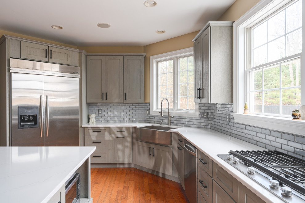 Example of a large transitional u-shaped medium tone wood floor and brown floor eat-in kitchen design with a farmhouse sink, shaker cabinets, gray cabinets, quartz countertops, gray backsplash, glass tile backsplash, stainless steel appliances, an island and white countertops