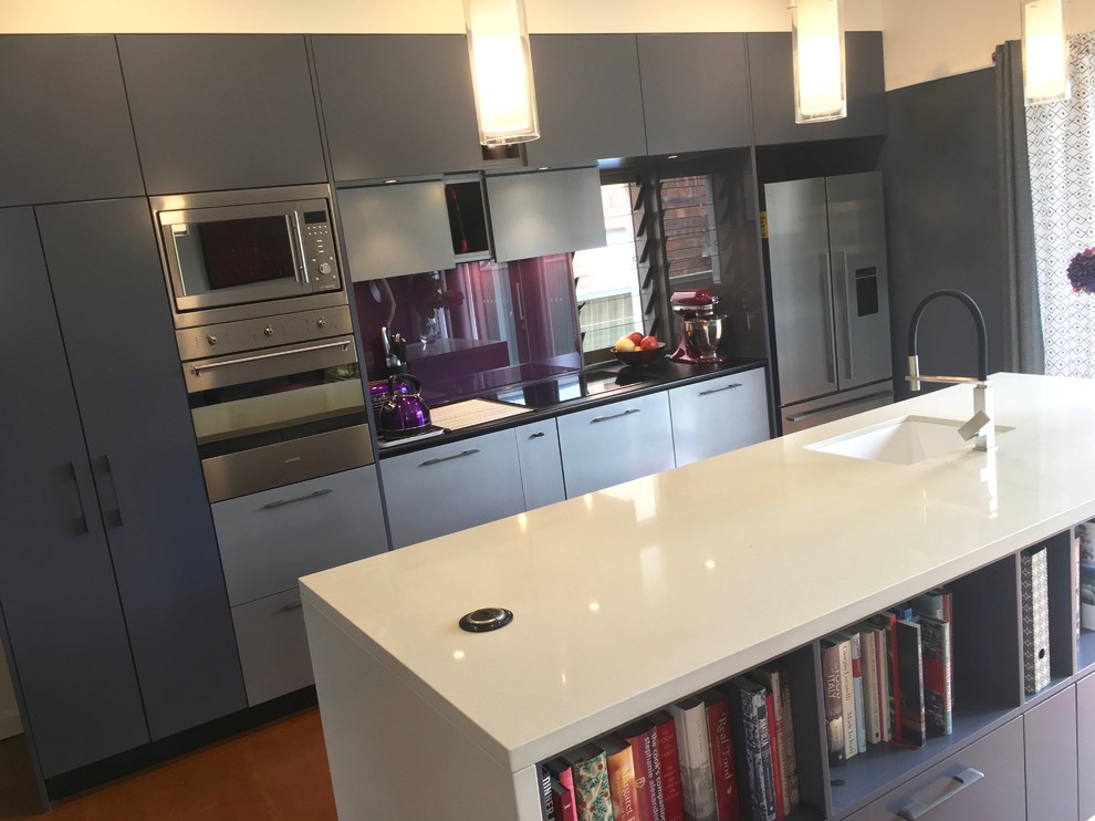 This is an example of a small modern galley open plan kitchen in Sydney with an undermount sink, flat-panel cabinets, blue cabinets, quartzite benchtops, metallic splashback, glass sheet splashback, stainless steel appliances, painted wood floors, with island, orange floor and white benchtop.