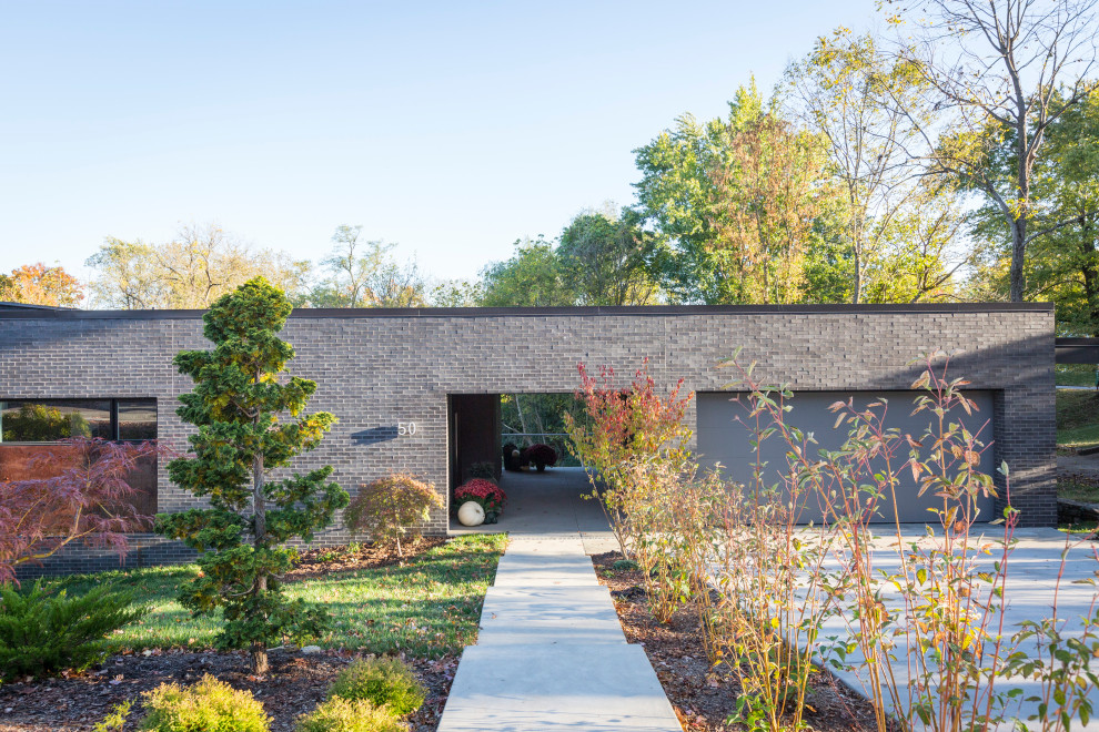 Réalisation d'une façade de maison noire minimaliste en brique à un étage avec un toit papillon.