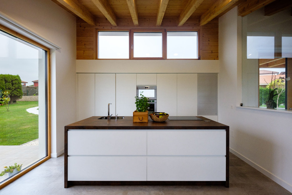 Contemporary kitchen in Other with an undermount sink, flat-panel cabinets, white cabinets, wood benchtops, stainless steel appliances, concrete floors, with island and grey floor.