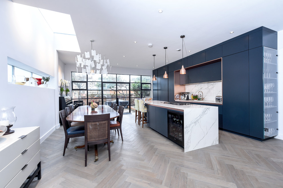 Photo of a mid-sized contemporary single-wall eat-in kitchen in London with flat-panel cabinets, blue cabinets, marble benchtops, white splashback, marble splashback, light hardwood floors, with island, white benchtop and beige floor.