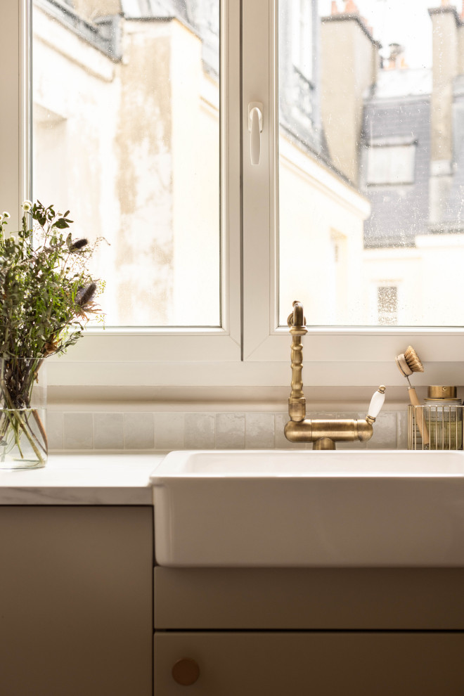 Réalisation d'une petite cuisine linéaire et beige et blanche nordique fermée avec un évier encastré, plan de travail en marbre, une crédence blanche, une crédence en céramique, un électroménager en acier inoxydable, un plan de travail blanc et fenêtre au-dessus de l'évier.