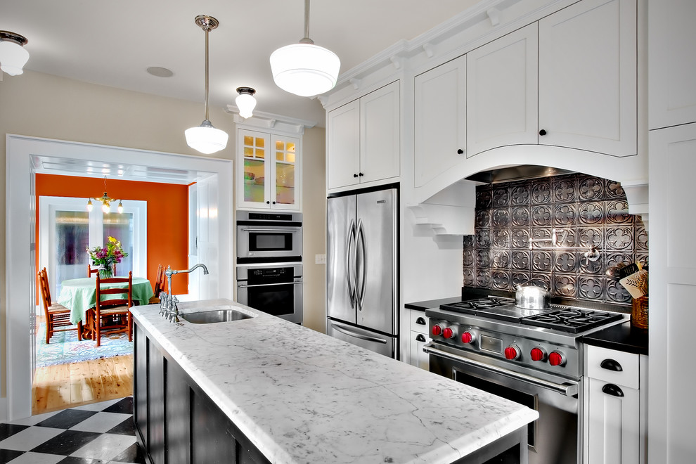 This is an example of an arts and crafts galley separate kitchen in Seattle with stainless steel appliances, an undermount sink, shaker cabinets, white cabinets, black splashback, metal splashback and marble benchtops.