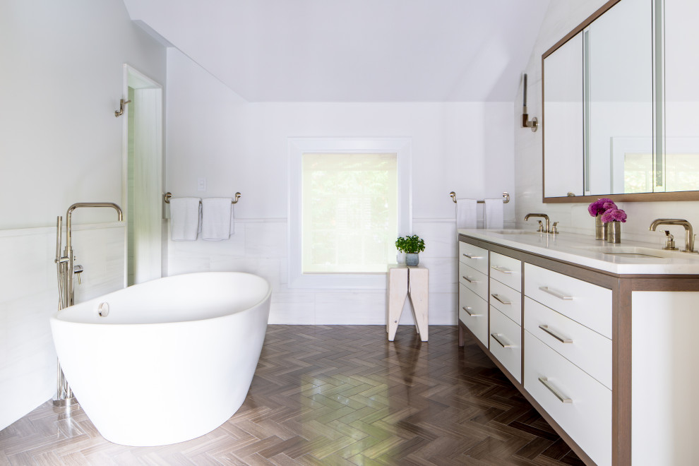 Photo of a transitional master bathroom in New York with furniture-like cabinets, medium wood cabinets, a freestanding tub, an alcove shower, a one-piece toilet, white tile, marble, white walls, wood-look tile, an undermount sink, quartzite benchtops, a hinged shower door, white benchtops, a shower seat, a double vanity and a freestanding vanity.