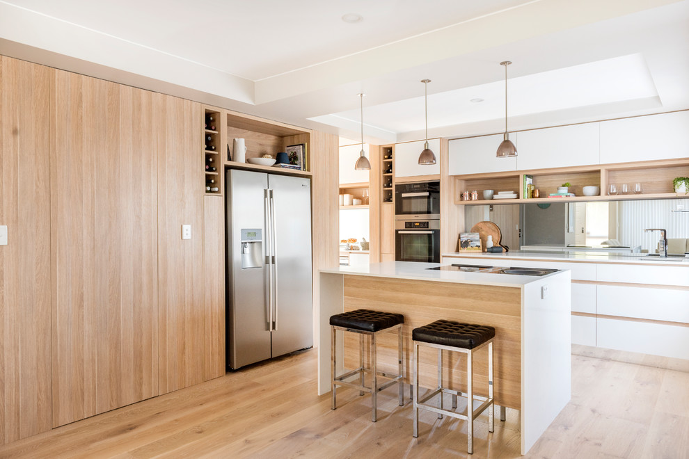 Photo of a mid-sized contemporary l-shaped open plan kitchen in Perth with light wood cabinets, with island, an undermount sink, flat-panel cabinets, mirror splashback, stainless steel appliances and light hardwood floors.