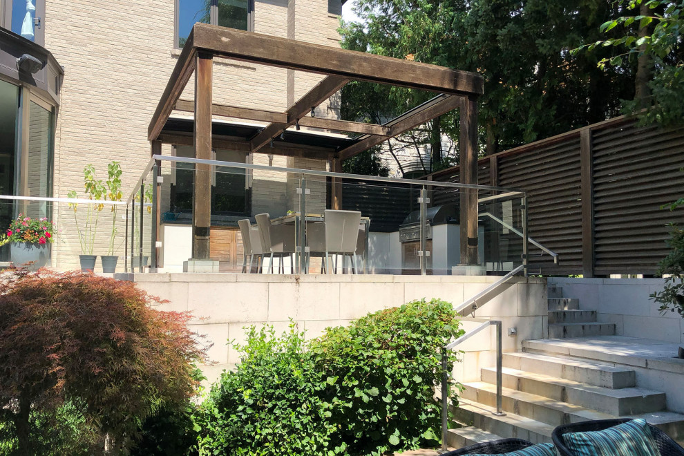 Photo of a contemporary backyard and first floor deck in Toronto with a pergola and glass railing.