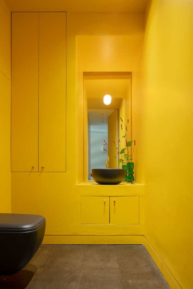 Photo of a small contemporary cloakroom in London with flat-panel cabinets, yellow cabinets, a one-piece toilet, yellow walls, concrete flooring, a vessel sink, grey floors, yellow worktops, a feature wall, a built in vanity unit and a drop ceiling.