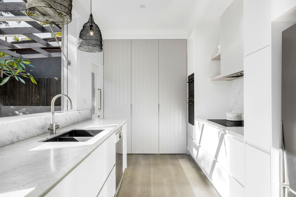 This is an example of a mid-sized beach style u-shaped eat-in kitchen in Sydney with an undermount sink, flat-panel cabinets, white cabinets, marble benchtops, grey splashback, marble splashback, stainless steel appliances, medium hardwood floors, no island, brown floor and grey benchtop.