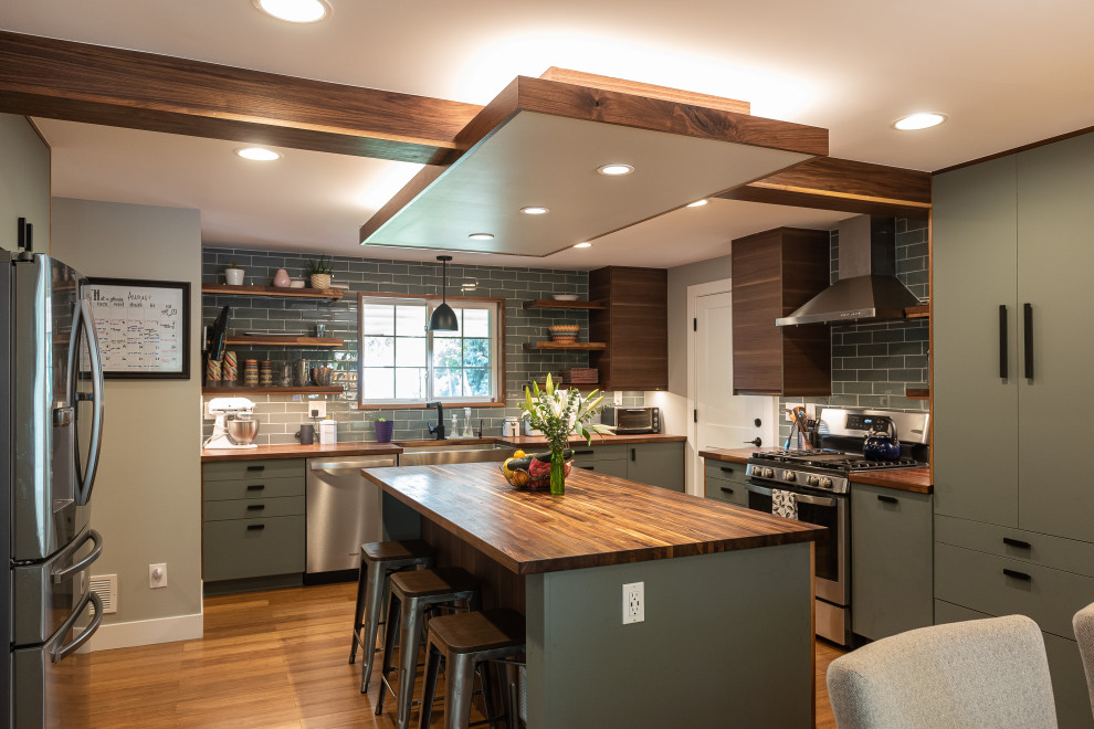 Design ideas for a large country u-shaped eat-in kitchen in Denver with a farmhouse sink, flat-panel cabinets, green cabinets, wood benchtops, grey splashback, subway tile splashback, stainless steel appliances, medium hardwood floors, with island, brown floor, brown benchtop and exposed beam.