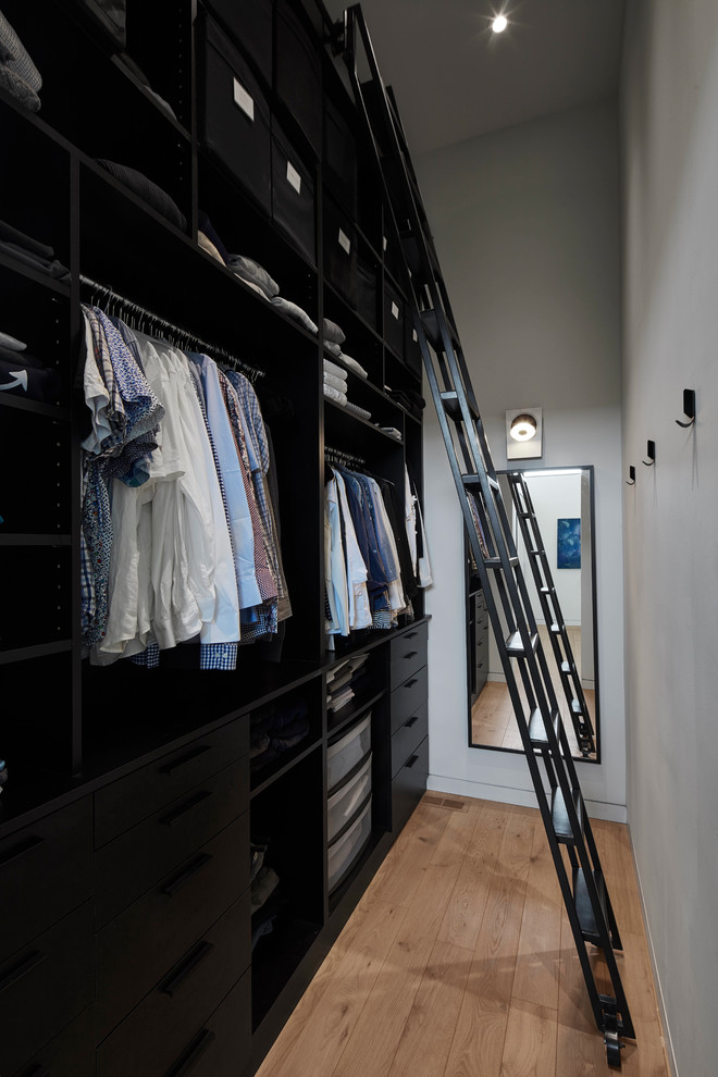 Photo of a contemporary men's walk-in wardrobe in Toronto with black cabinets, light hardwood floors and beige floor.