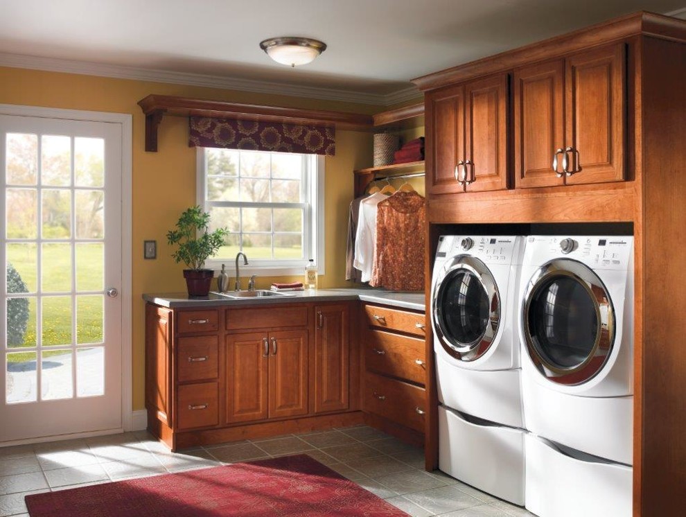 Design ideas for a mid-sized traditional l-shaped dedicated laundry room in Nashville with a drop-in sink, raised-panel cabinets, medium wood cabinets, quartz benchtops, yellow walls, ceramic floors, a side-by-side washer and dryer, grey floor and grey benchtop.