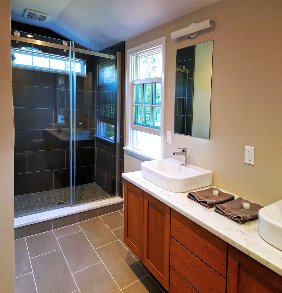 Mid-sized transitional master porcelain tile and brown floor alcove shower photo with shaker cabinets, medium tone wood cabinets, a vessel sink, beige walls, a hinged shower door and white countertops