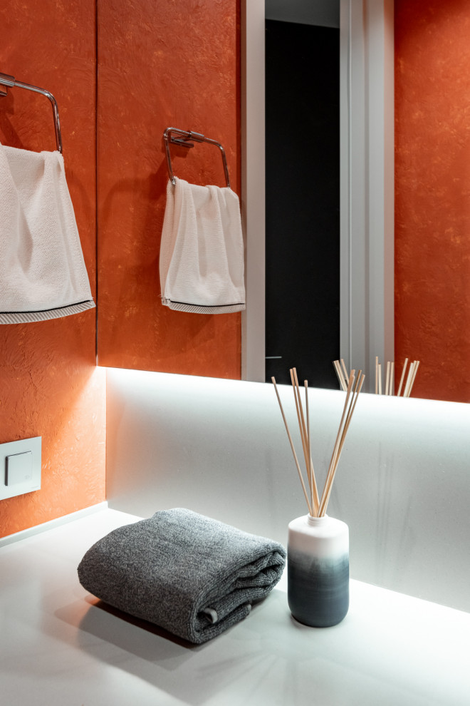 Inspiration for a small modern powder room in Yekaterinburg with flat-panel cabinets, orange cabinets, a wall-mount toilet, orange walls, vinyl floors, an undermount sink, solid surface benchtops, beige floor, grey benchtops and a built-in vanity.