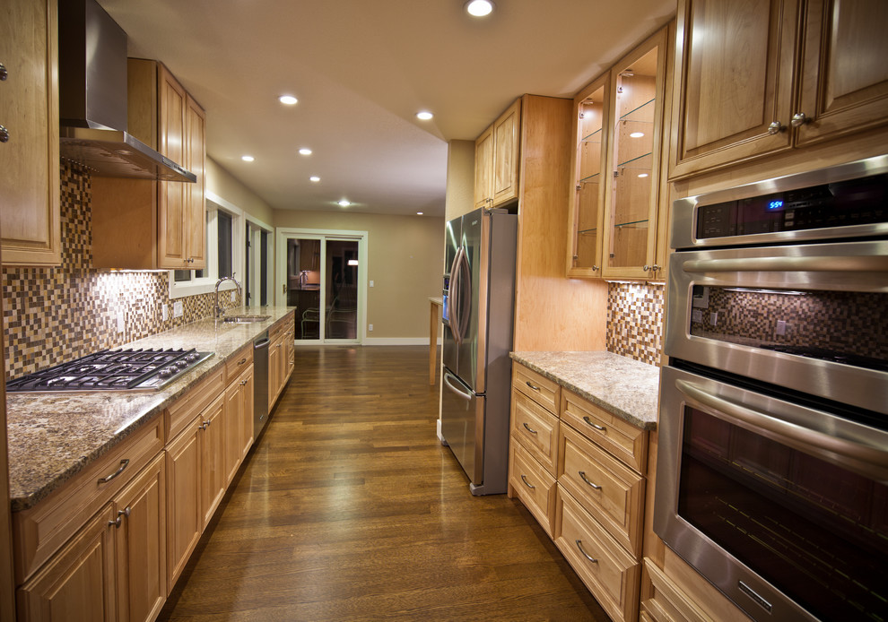 Enclosed kitchen - mid-sized transitional galley medium tone wood floor and brown floor enclosed kitchen idea in Denver with a double-bowl sink, raised-panel cabinets, medium tone wood cabinets, granite countertops, multicolored backsplash, mosaic tile backsplash, stainless steel appliances and no island