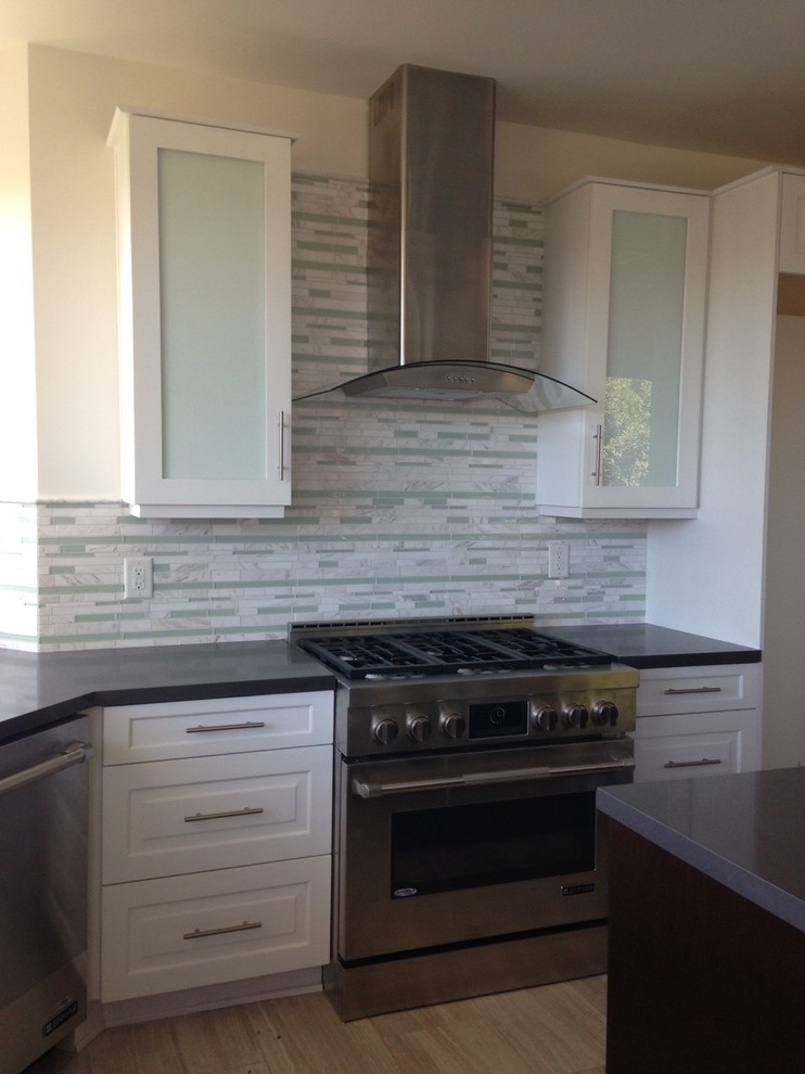 Eat-in kitchen - mid-sized transitional l-shaped travertine floor eat-in kitchen idea in Los Angeles with white cabinets, solid surface countertops, multicolored backsplash, stainless steel appliances, an island, marble backsplash and recessed-panel cabinets