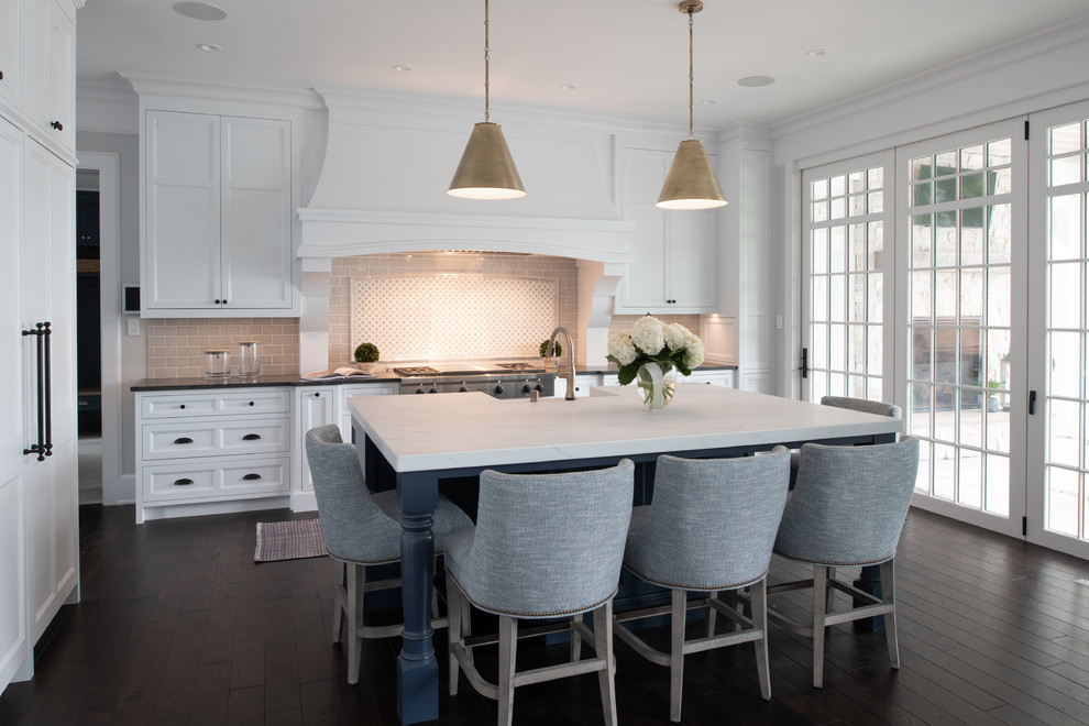 Inspiration for a mid-sized transitional l-shaped kitchen in Minneapolis with a farmhouse sink, recessed-panel cabinets, white cabinets, quartz benchtops, beige splashback, subway tile splashback, stainless steel appliances, dark hardwood floors, with island, brown floor and white benchtop.