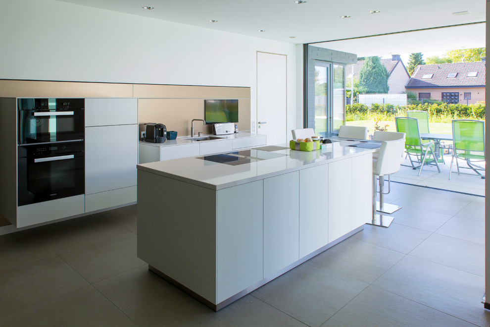 Photo of a large modern galley eat-in kitchen in Dortmund with a drop-in sink, flat-panel cabinets, white cabinets, metallic splashback, black appliances and with island.