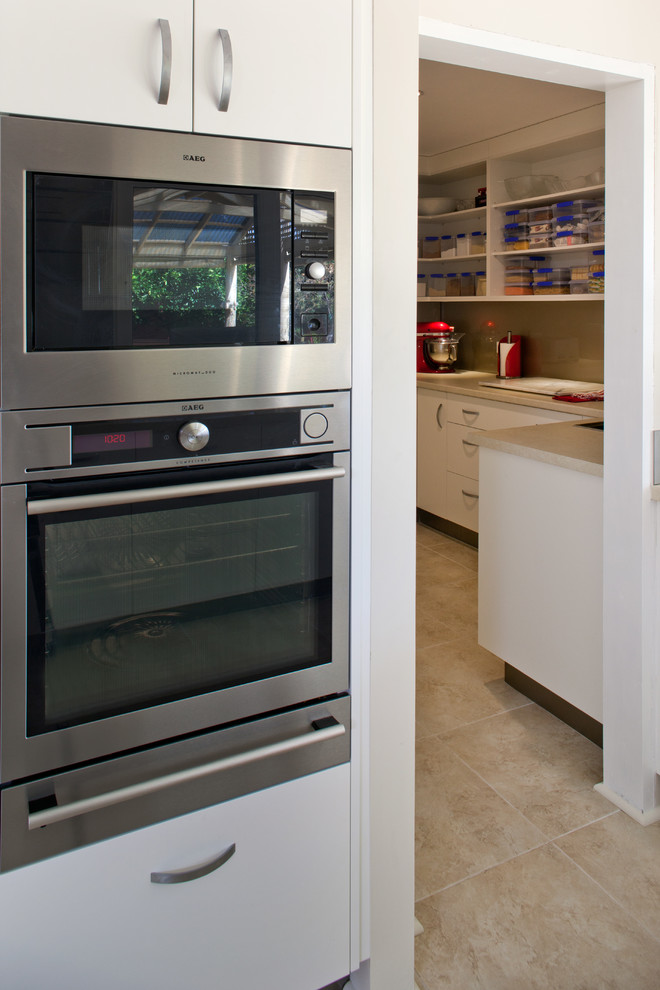 Modern kitchen in Perth with flat-panel cabinets, white cabinets, quartz benchtops, brown splashback, glass sheet splashback, stainless steel appliances and beige benchtop.