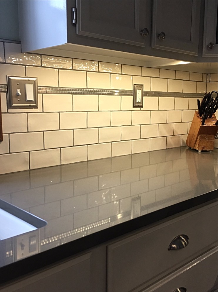Example of a mid-sized transitional u-shaped medium tone wood floor enclosed kitchen design with an undermount sink, white cabinets, quartz countertops, white backsplash, subway tile backsplash, stainless steel appliances and an island