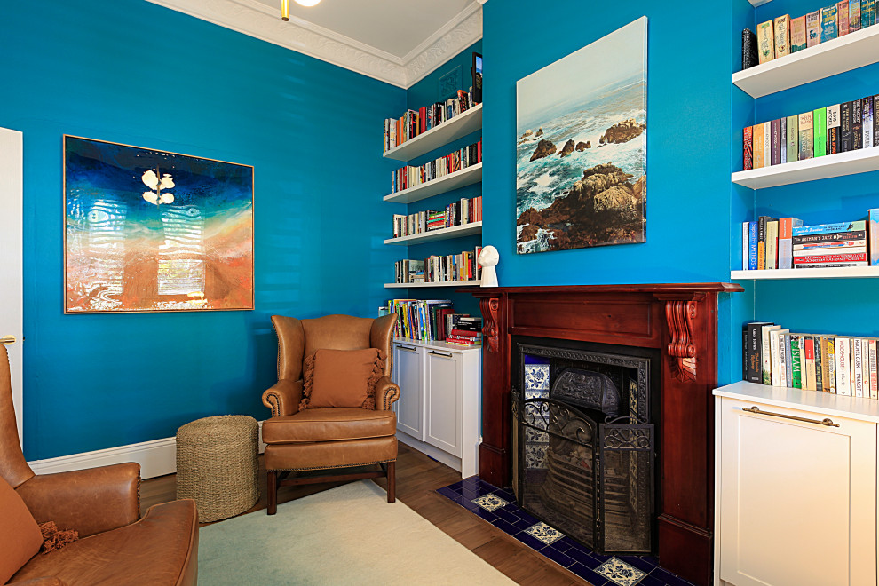 This is an example of a small transitional guest bedroom in Sydney with blue walls, medium hardwood floors, a standard fireplace, a wood fireplace surround and brown floor.