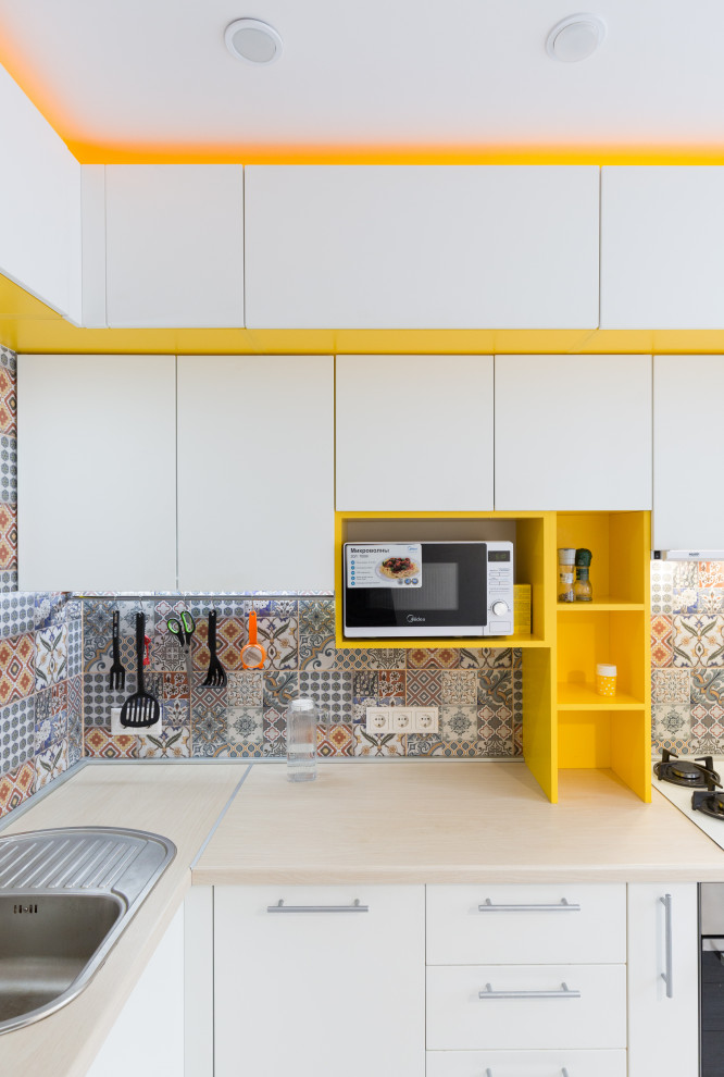 This is an example of a small contemporary l-shaped separate kitchen in Other with a single-bowl sink, flat-panel cabinets, white cabinets, wood benchtops, multi-coloured splashback, ceramic splashback, stainless steel appliances, laminate floors, beige floor and beige benchtop.