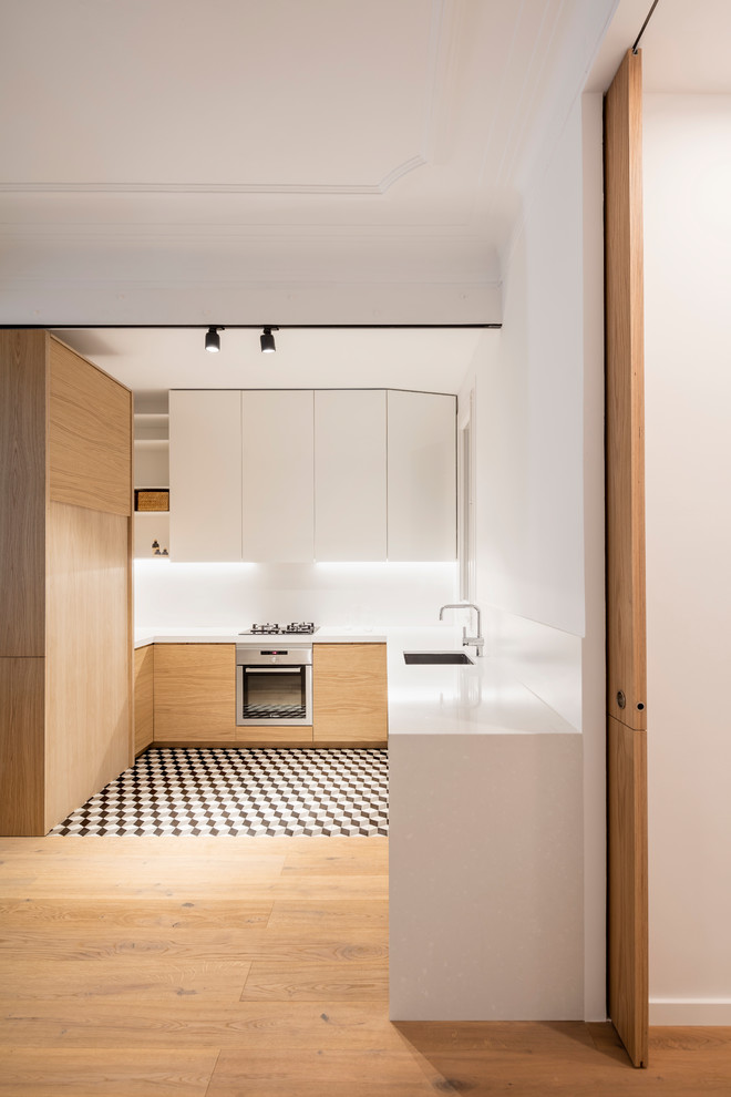 This is an example of a mid-sized scandinavian u-shaped kitchen in Barcelona with flat-panel cabinets, white splashback, stainless steel appliances, ceramic floors, no island, multi-coloured floor, a single-bowl sink and white cabinets.