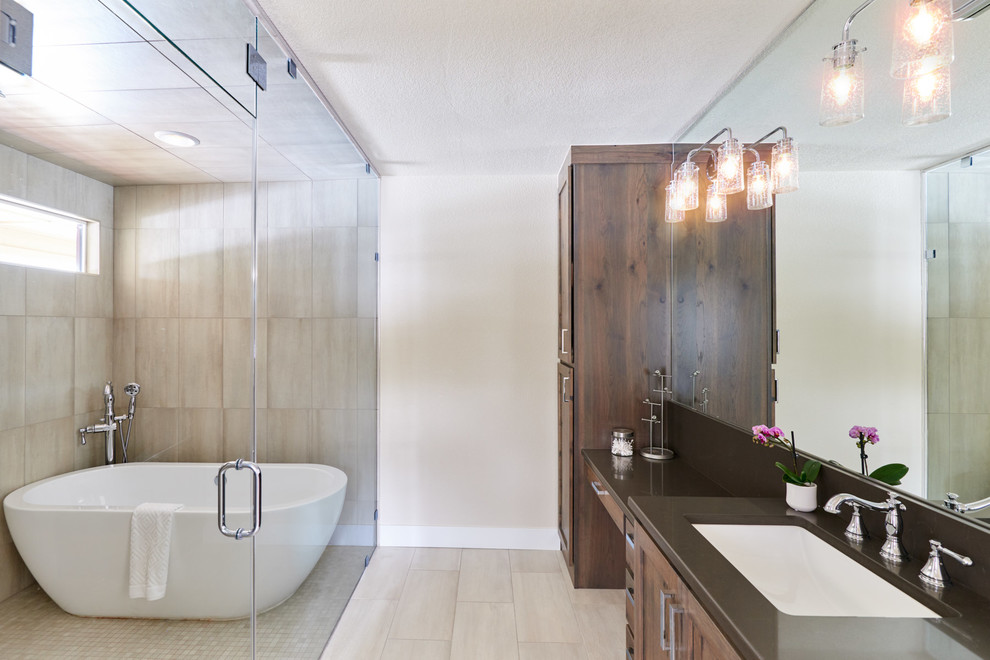 Large transitional master wet room bathroom in Denver with shaker cabinets, brown cabinets, a freestanding tub, a two-piece toilet, gray tile, ceramic tile, beige walls, ceramic floors, an undermount sink, engineered quartz benchtops, beige floor, a hinged shower door and black benchtops.