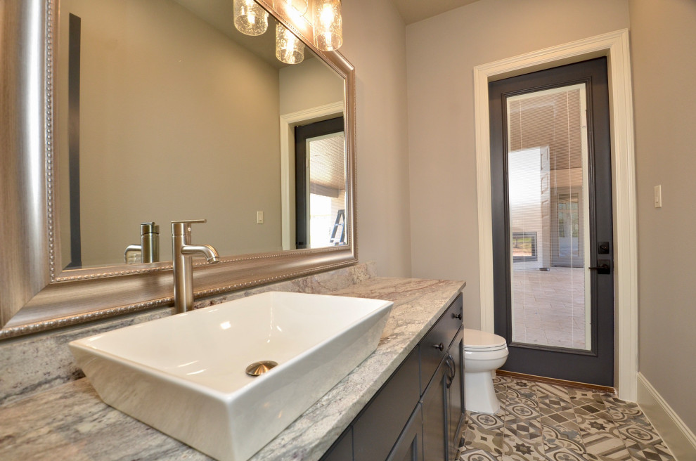 Photo of a mid-sized transitional powder room in Houston with flat-panel cabinets, grey cabinets, a two-piece toilet, grey walls, porcelain floors, a vessel sink, granite benchtops, grey floor and white benchtops.