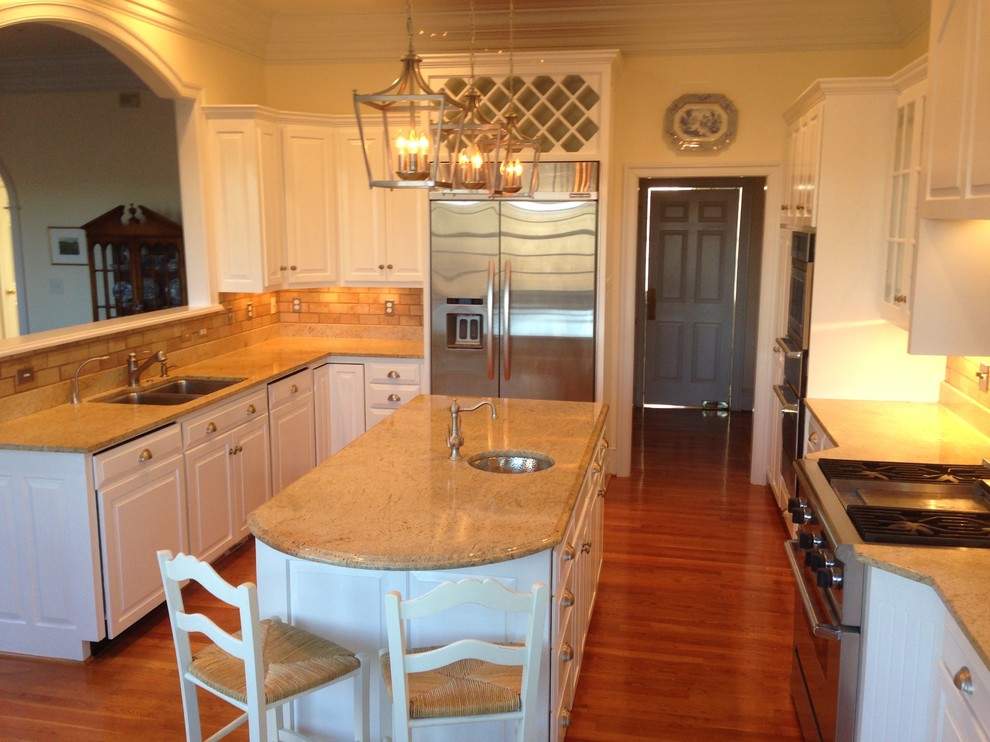Mid-sized transitional l-shaped medium tone wood floor enclosed kitchen photo with an undermount sink, raised-panel cabinets, white cabinets, granite countertops, beige backsplash, stone tile backsplash, stainless steel appliances and an island