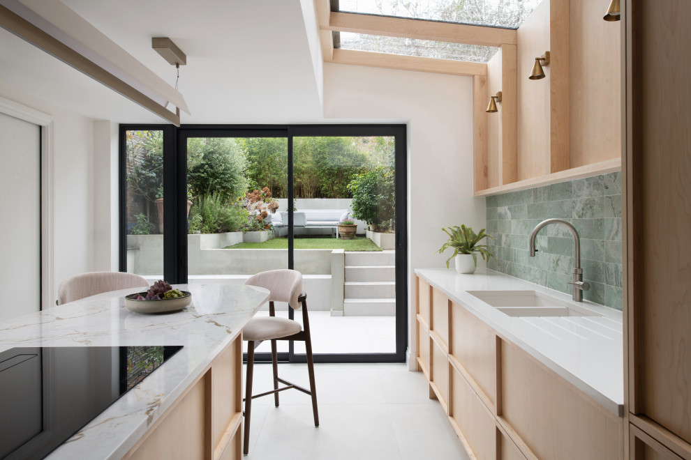 Inspiration for a mid-sized contemporary single-wall eat-in kitchen in London with raised-panel cabinets, light wood cabinets, quartzite benchtops, green splashback, marble splashback, stainless steel appliances, porcelain floors, with island, grey floor and white benchtop.