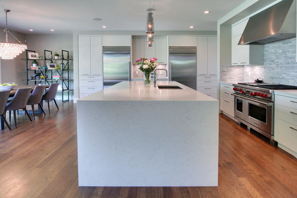 Transitional medium tone wood floor and brown floor kitchen photo in Calgary with an undermount sink, flat-panel cabinets, quartz countertops, gray backsplash, marble backsplash, stainless steel appliances and an island