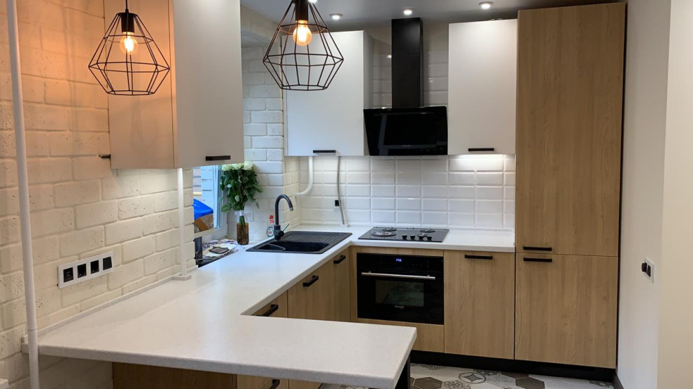 Small industrial u-shaped open plan kitchen in Moscow with a single-bowl sink, flat-panel cabinets, medium wood cabinets, solid surface benchtops, white splashback, porcelain splashback, black appliances, porcelain floors, no island, grey floor and white benchtop.