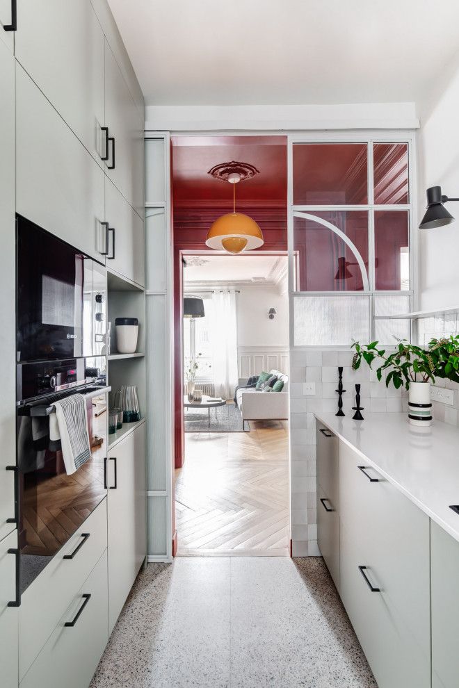 Mid-sized contemporary l-shaped separate kitchen in Paris with an undermount sink, flat-panel cabinets, green cabinets, quartz benchtops, white splashback, black appliances, terrazzo floors, white floor and white benchtop.