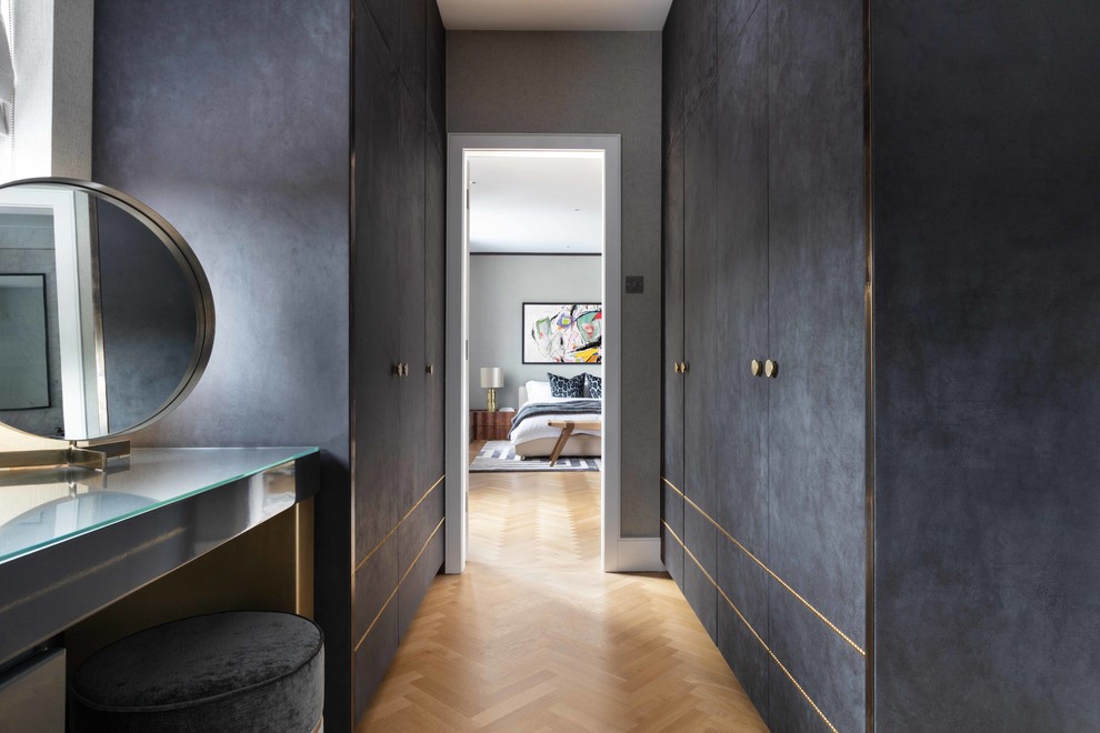 This is an example of a large contemporary gender-neutral dressing room in London with flat-panel cabinets, black cabinets, medium hardwood floors and brown floor.