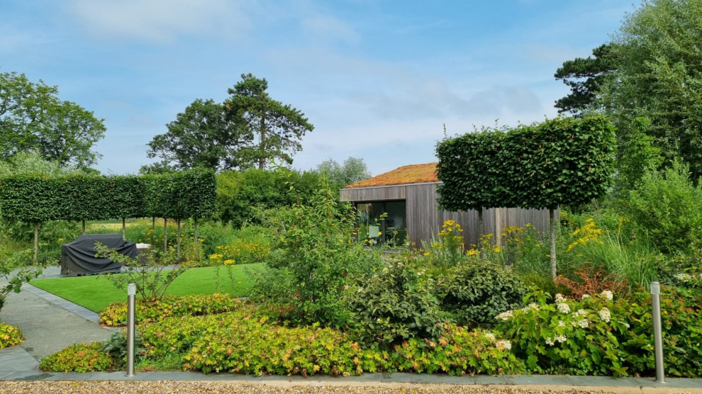 Modern inredning av en mycket stor formell trädgård, med en stödmur och naturstensplattor